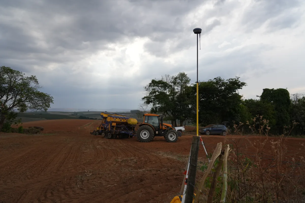CHCNAV RTK base station receiver on a pole at a field edge with a tractor and planter working behind it