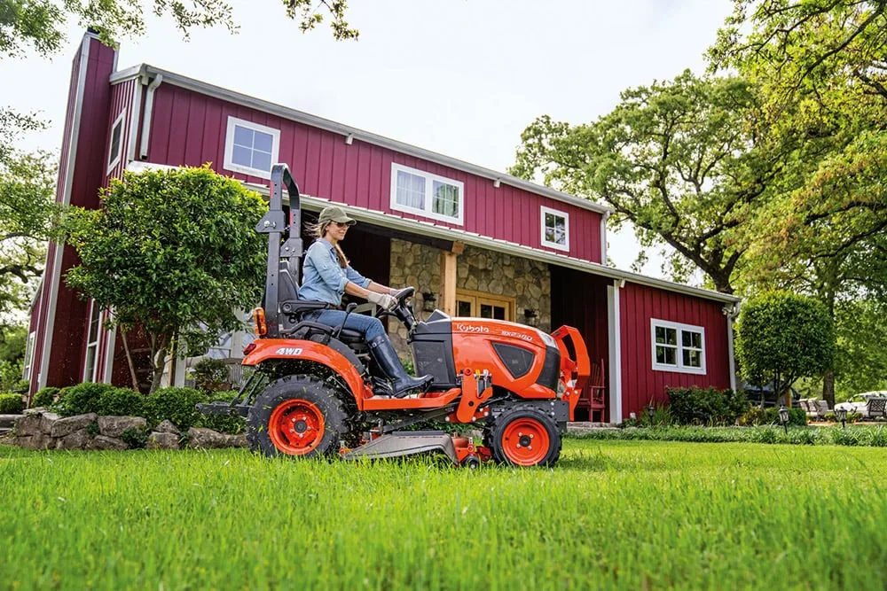 Kubota BX2380 sub-compact tractor mowing a lawn with a mid-mount mower deck