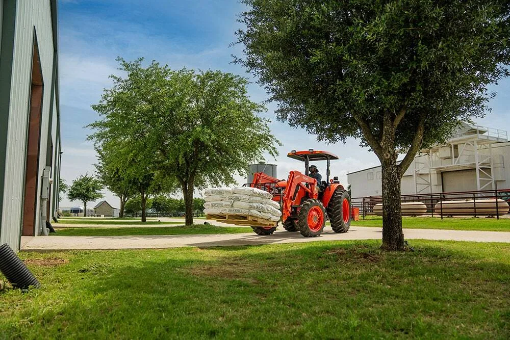 Kubota M6060 utility tractor carrying bagged feed on loader-mounted pallet forks